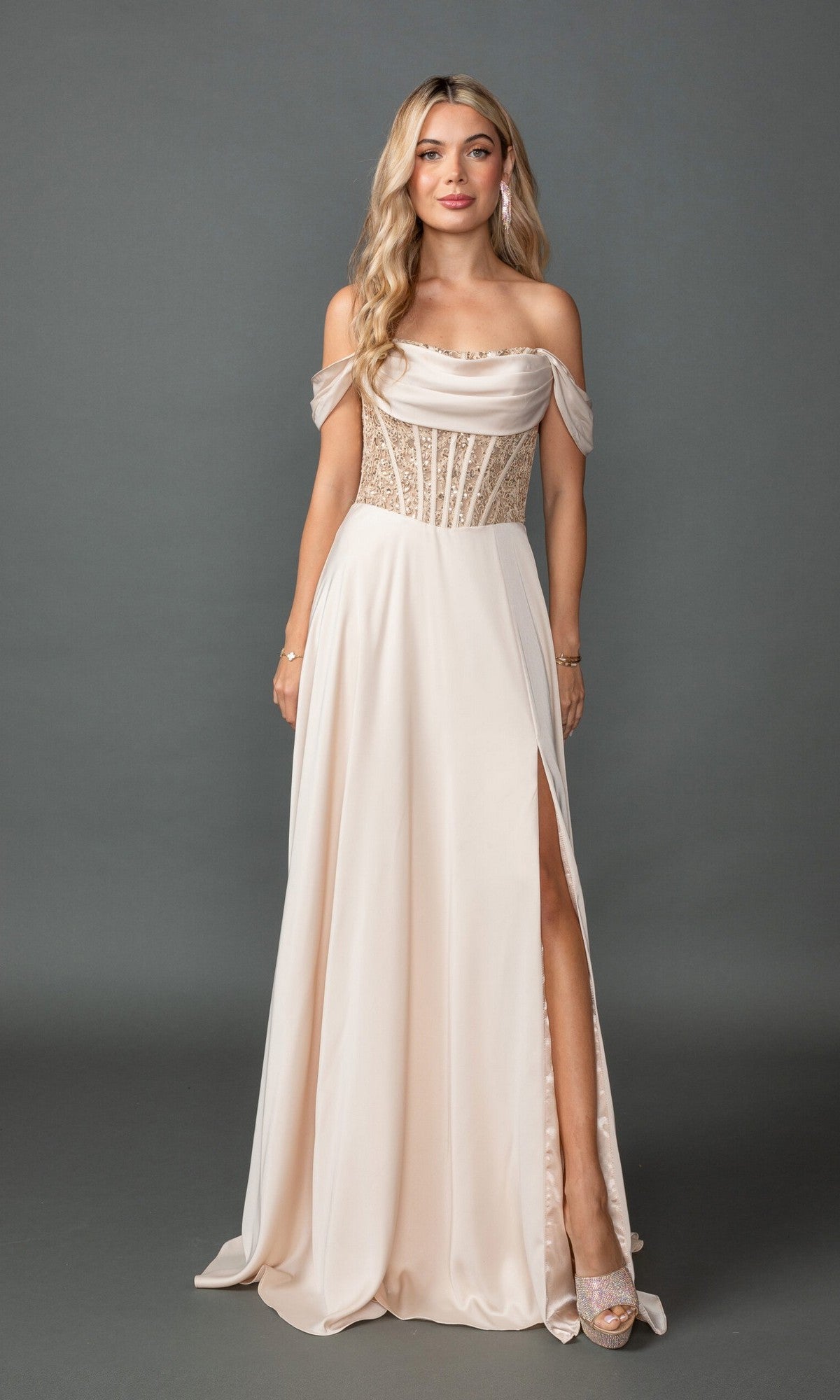 A woman models the Off-Shoulder Corset Prom Gown: Dancing Queen 4546A, featuring a sheer embellished bodice and thigh-high slit, as she poses against a plain gray background.